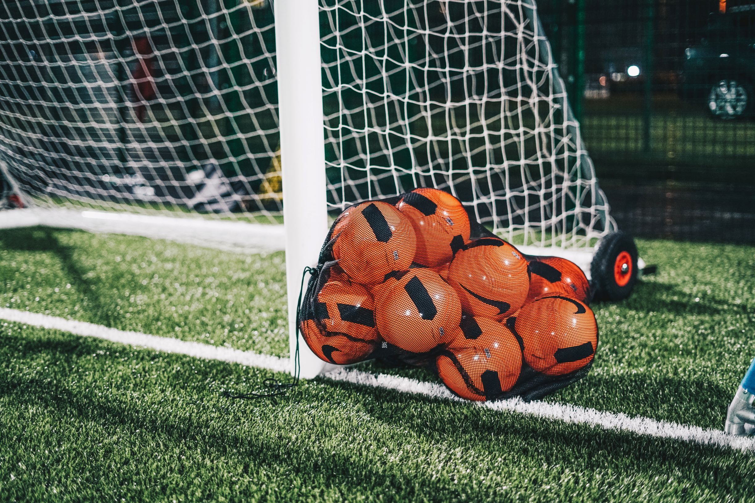 Footballs in a bag sitting next to a goal ready for a training session